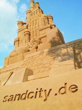 Blick von unten auf eine große Sandskulptur. Unten steht sandcity.de