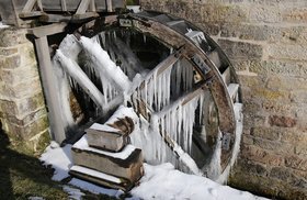 Ein Wasserrad ist festgefroren. Eiszapfen hängen an den Holzstreben.