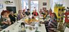 Eine Gruppe kostümierter Seniorinnen und Senioren sitzt bei bester Laune um einen Tisch. 